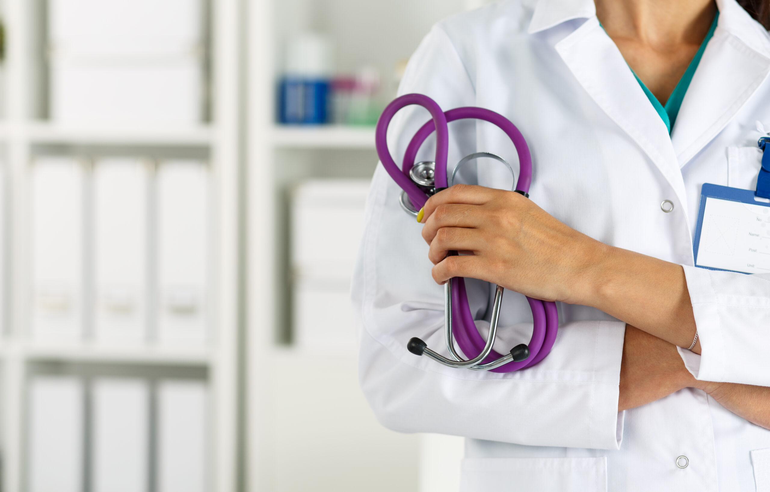 A healthcare professional in a lab coat holds a purple stethoscope, standing in a clinical setting to signify medical expertise and care.
